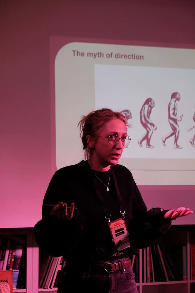 Woman presenting on human evolution and movement with a slide titled "The myth of direction".
