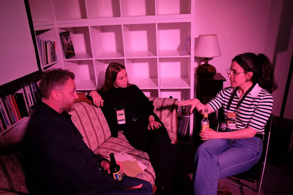 Three people having a conversation in a cozy, pink-lit room at Coffeehouse Conference.