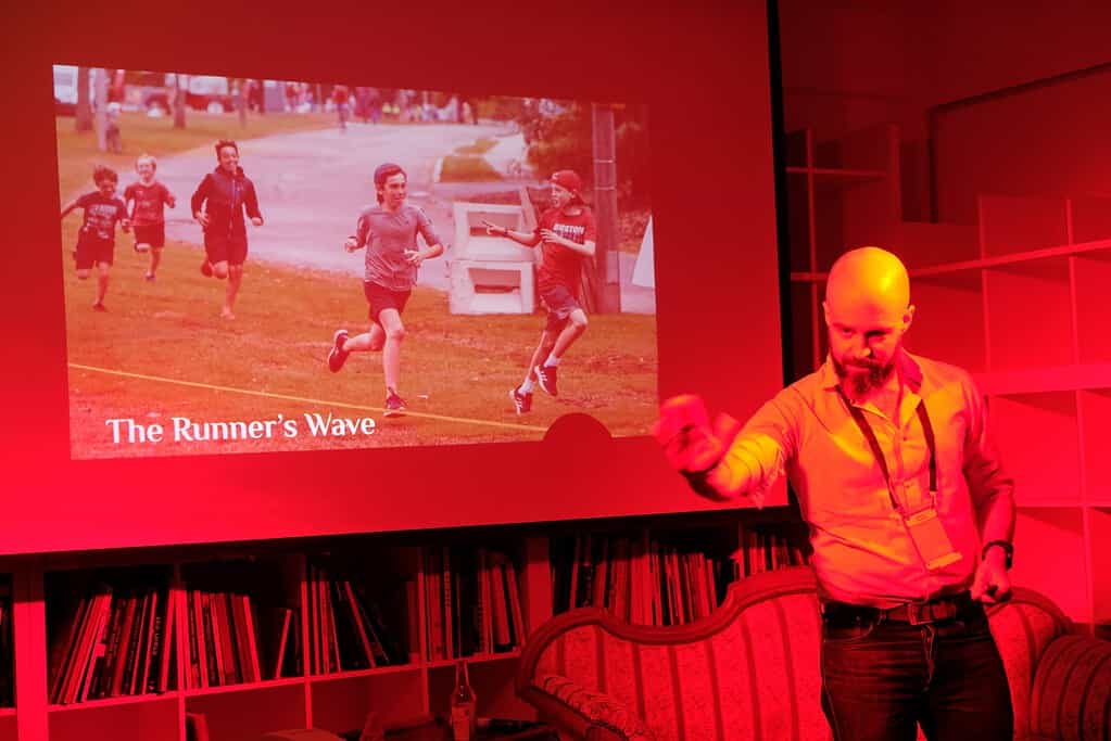 Man presenting on stage with a slide titled "The Runner's Wave" at Coffeehouse Conference.