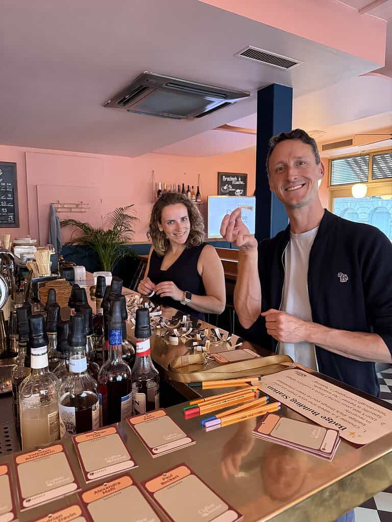 Two smiling people at a bar with bottles and cards during Coffeehouse Conference.