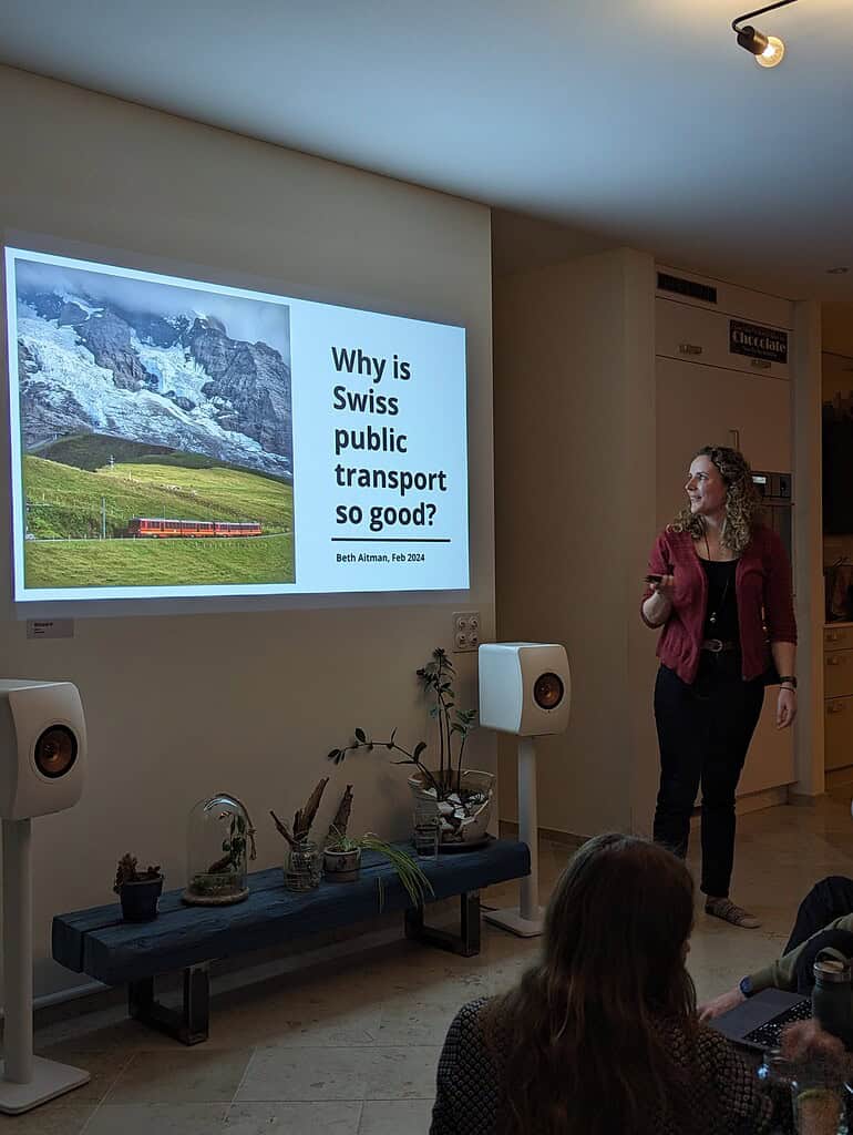 Woman presenting on Swiss public transport benefits during Coffeehouse Conference event.